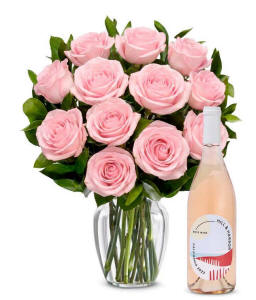 A bouquet of 12 soft pink roses arranged in a clear glass vase is displayed next to a bottle of Hill &amp; Harbor California Ros&eacute;.